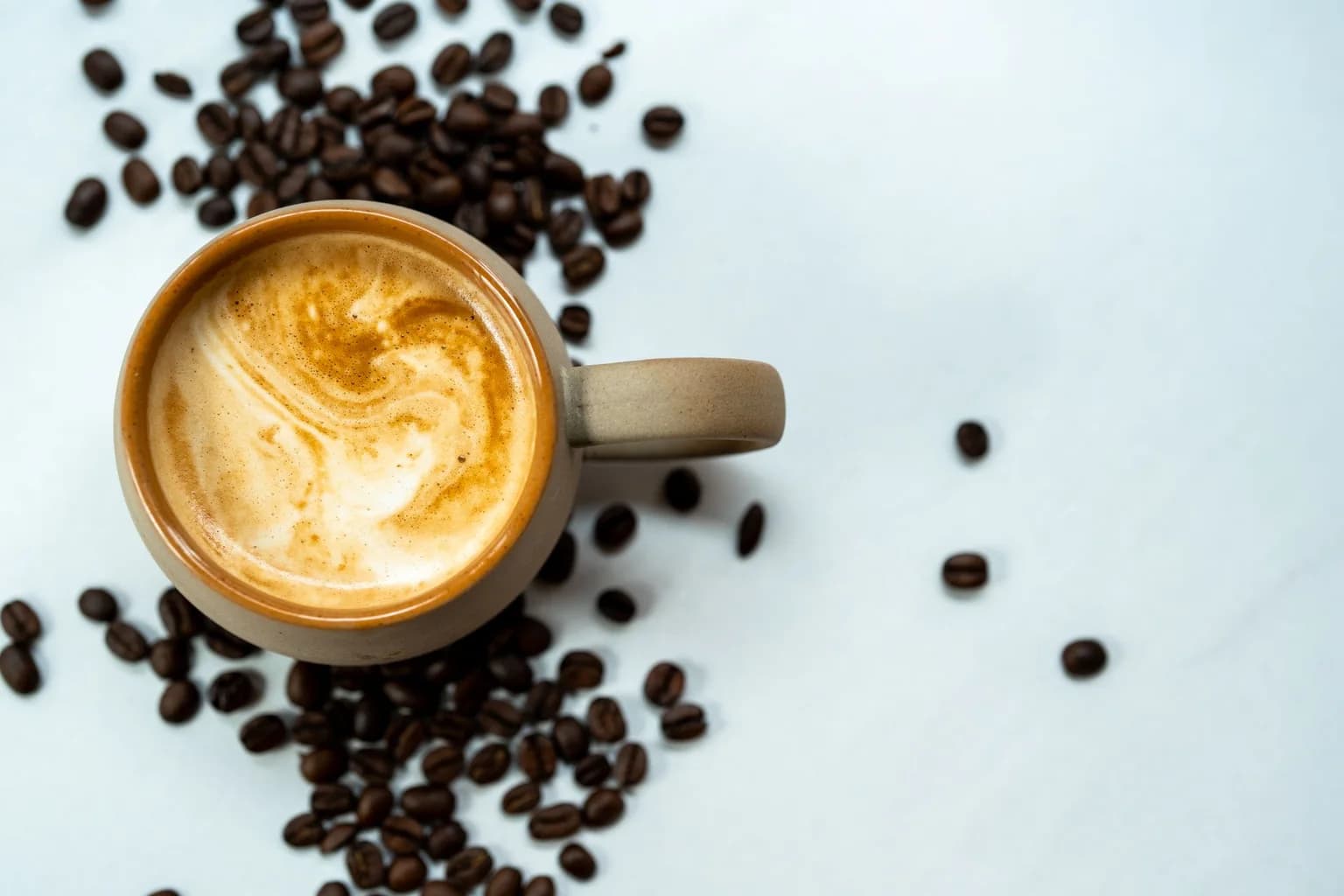 A cup of coffee surrounded by roasted coffee beans