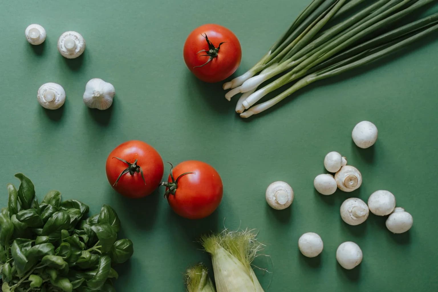 Tomatoes, mushrooms, spring onions and basil arranged on a green surface