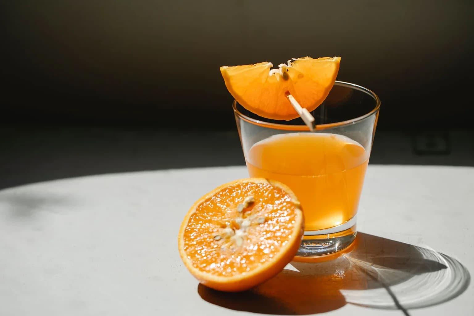 A glass of orange juice beside freshly cut orange slices